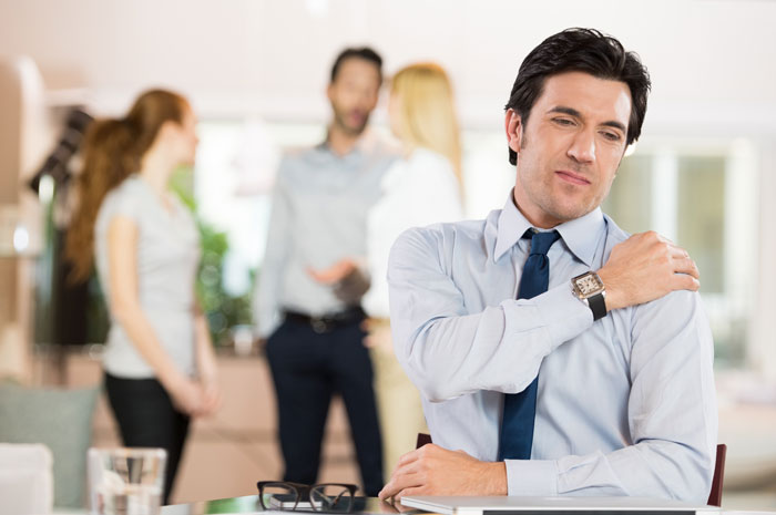 man rubbing sore shoulder while sitting at a desk at work