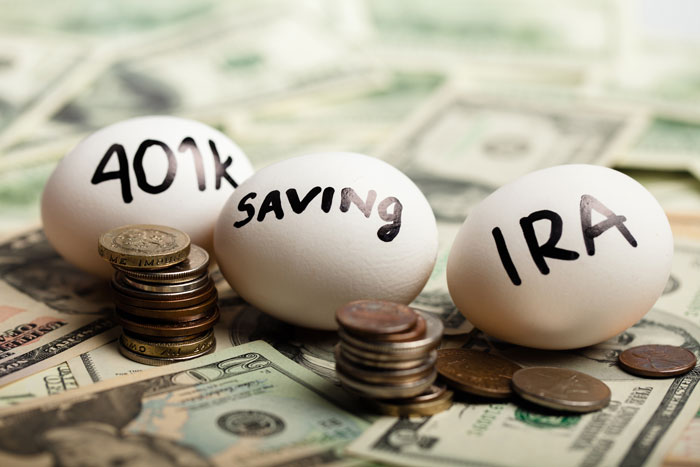 Three eggs with 401(k) saving and IRA written on them laying on top of dollar bills and coins